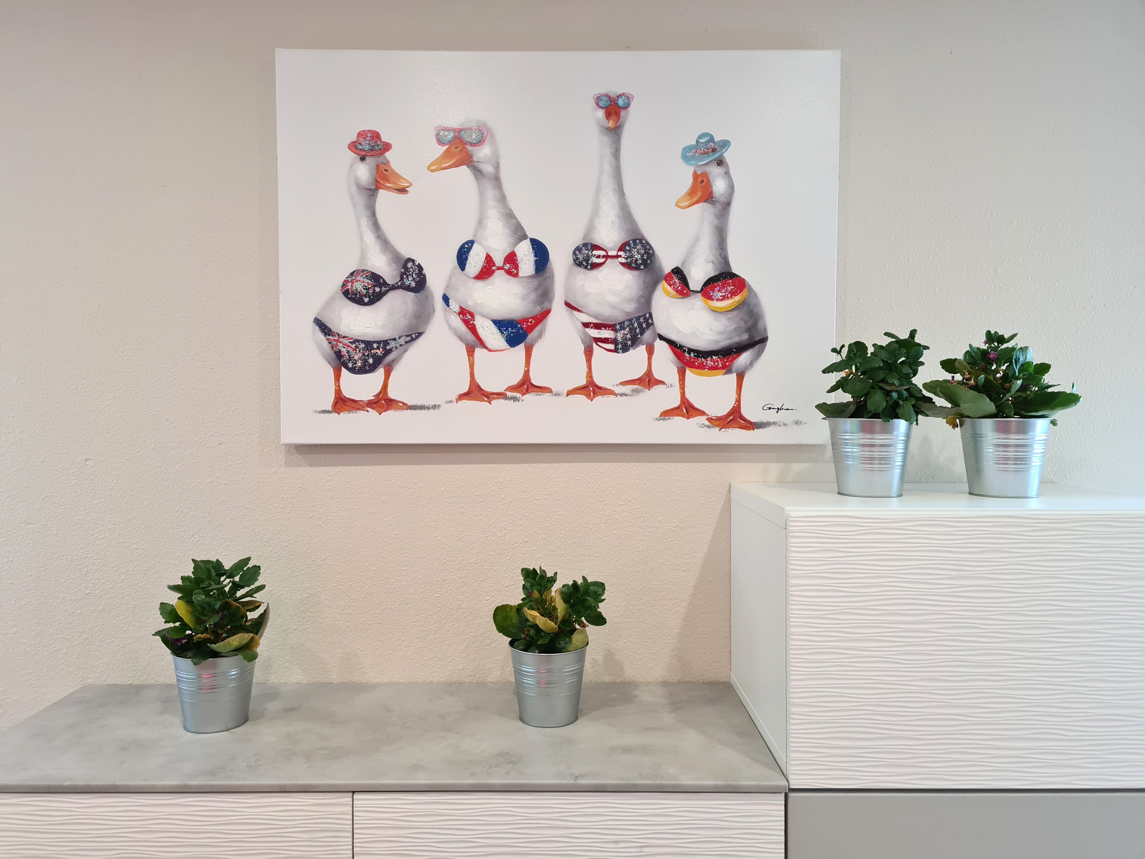 Un cuadro muestra cuatro gansos con accesorios, colgado en una pared, flanqueado por macetas con plantas sobre un estante blanco.