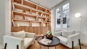 A modern living room with two sofas, a coffee table, and a wooden shelving unit with various decorative items. - Alexandrine Opera (Paris)