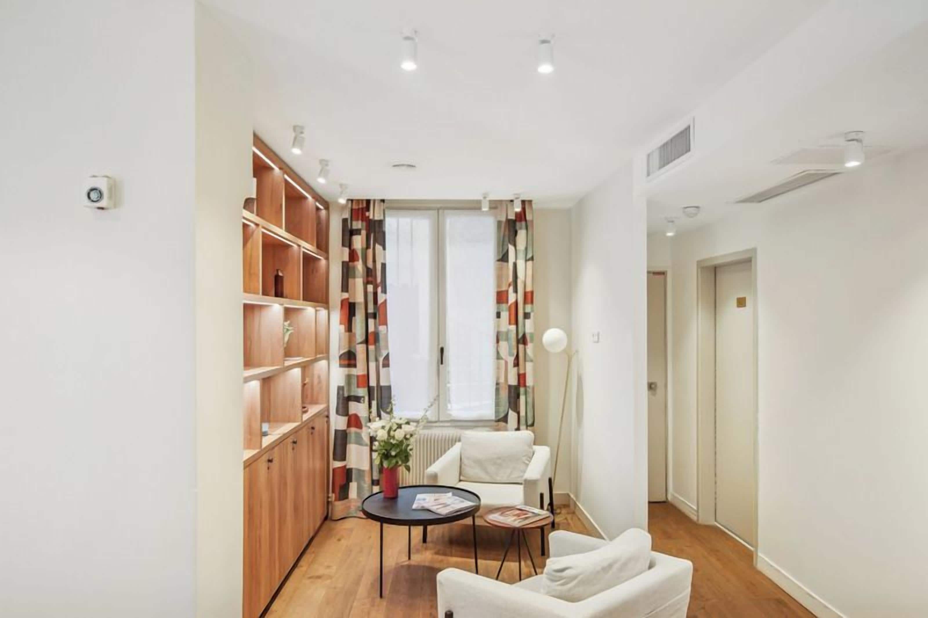 A modern interior with a wooden shelving unit, a white armchair, a small round table with a vase, and a floor lamp.