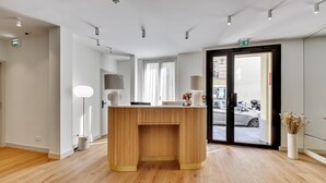 A reception desk with a wooden finish, a white wall, and a large window with curtains. - Alexandrine Opera (Paris)
