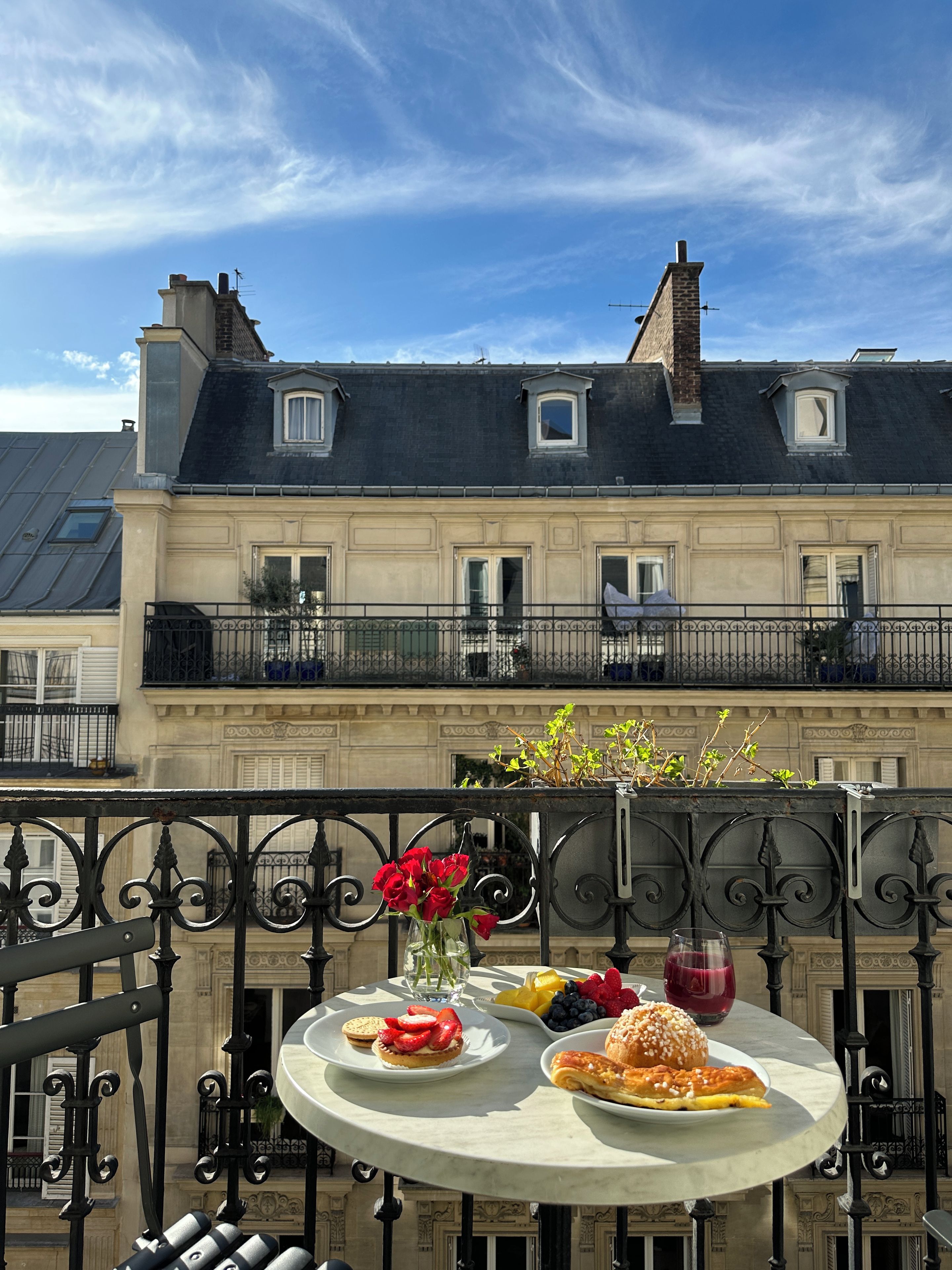 A balcony with a table set for breakfast, overlooking a building with a mansard roof.