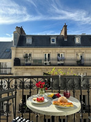 A balcony with a table set for breakfast, overlooking a building with a mansard roof. - Alexandrine Opera (Paris)
