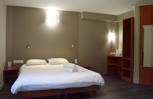 A hotel room with a large bed, two bedside tables, a wardrobe, and a mirror.