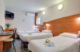 A hotel room with two single beds, a desk with a laptop, a chair, a TV mounted on the wall, and a window with curtains.