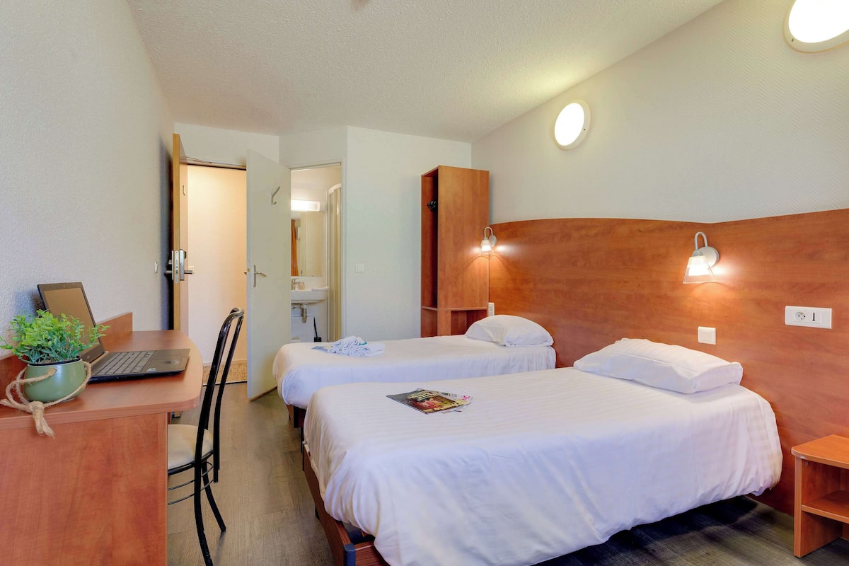 Habitación de hotel con dos camas, un escritorio con una computadora portátil, una silla y una mesita.