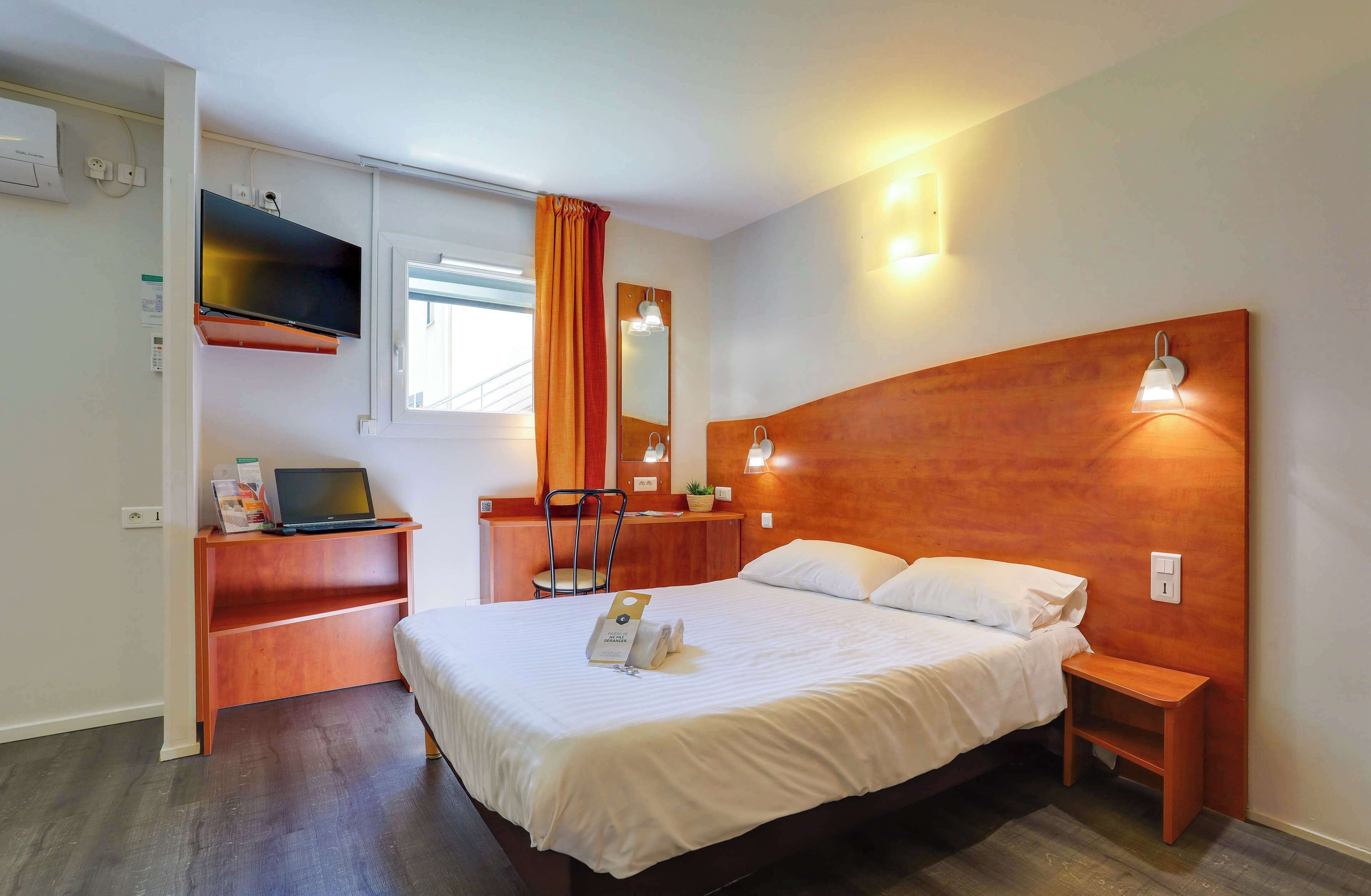 Habitación de hotel con cama, escritorio, computadora portátil, espejo y televisor en la pared.