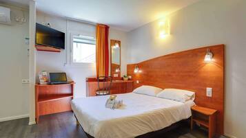 Habitación de hotel con cama, escritorio, computadora portátil, espejo y televisor en la pared.