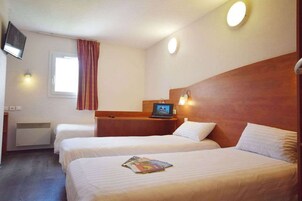 Une chambre d’hôtel avec deux lits, une télévision, un bureau avec un ordinateur portable et une fenêtre avec des rideaux.