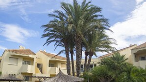 A resort with multiple buildings, palm trees, and a thatched umbrella structure. - Aparthotel Villas La Manga (Cartagena)