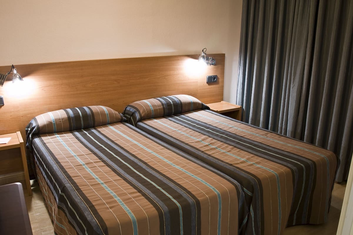 Un lit double avec une literie à rayures, deux tables de chevet avec des lampes, une tête de lit en bois et un rideau sur le côté droit.