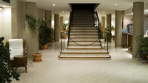 A grand staircase in a hotel lobby with marble steps, surrounded by large columns and potted plants. - Aparthotel Villas La Manga (Cartagena)