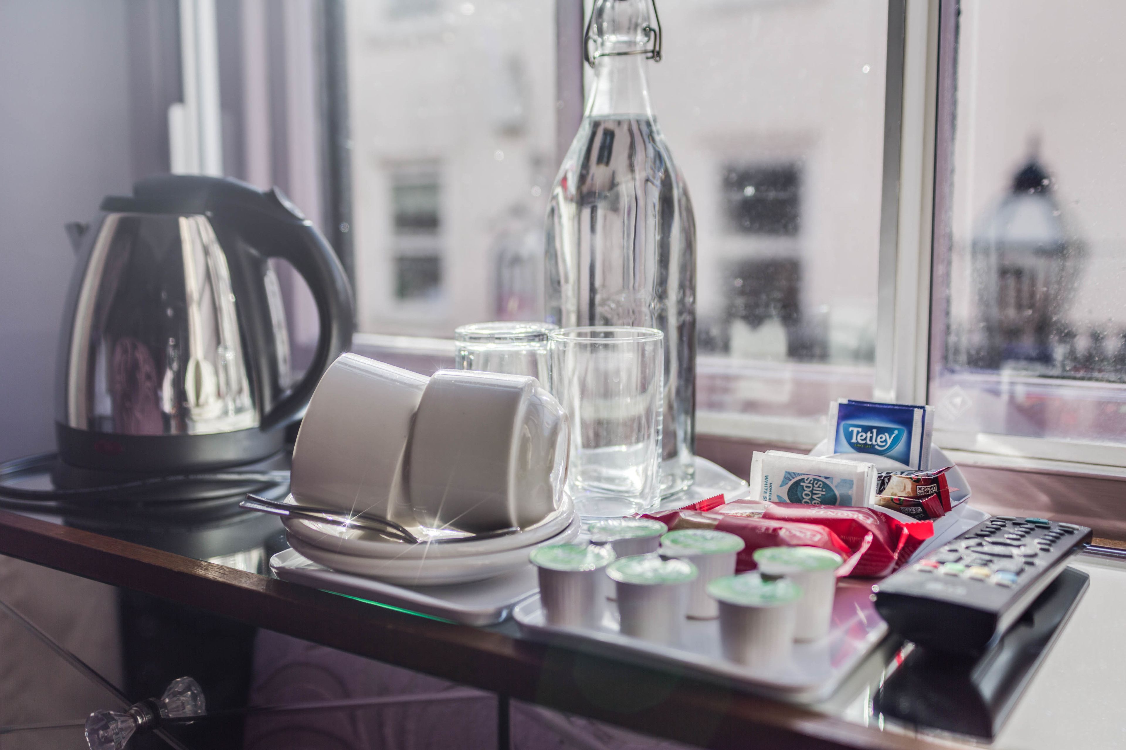 Hotelkamer met uitzicht uit het raam, een waterkoker, glazen, een fles, een dienblad met toevoegingen en een afstandsbediening.