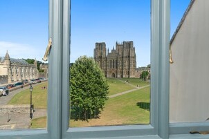 Vista de una catedral histórica a través de una ventana, con cielo despejado y un árbol en primer plano.