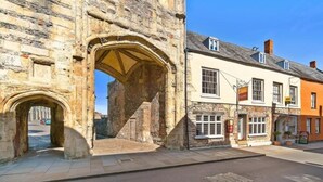 A stone archway leading to a street with a building that has multiple windows and a signboard. - The Ancient Gatehouse Hotel (Wells)