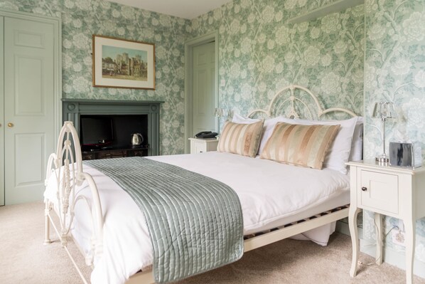 A bedroom with a bed, nightstands, a fireplace, and floral wallpaper. - The Ancient Gatehouse Hotel (Wells)
