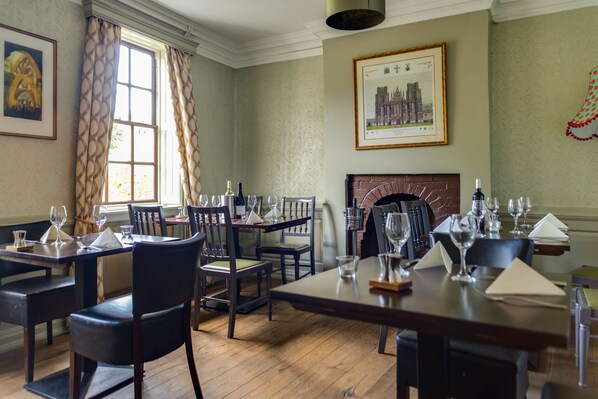 A dining room with tables set for a meal, chairs, a fireplace, and framed pictures on the walls. - The Ancient Gatehouse Hotel (Wells)