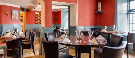 A dining area with round tables and black chairs, red walls, and wooden floors.