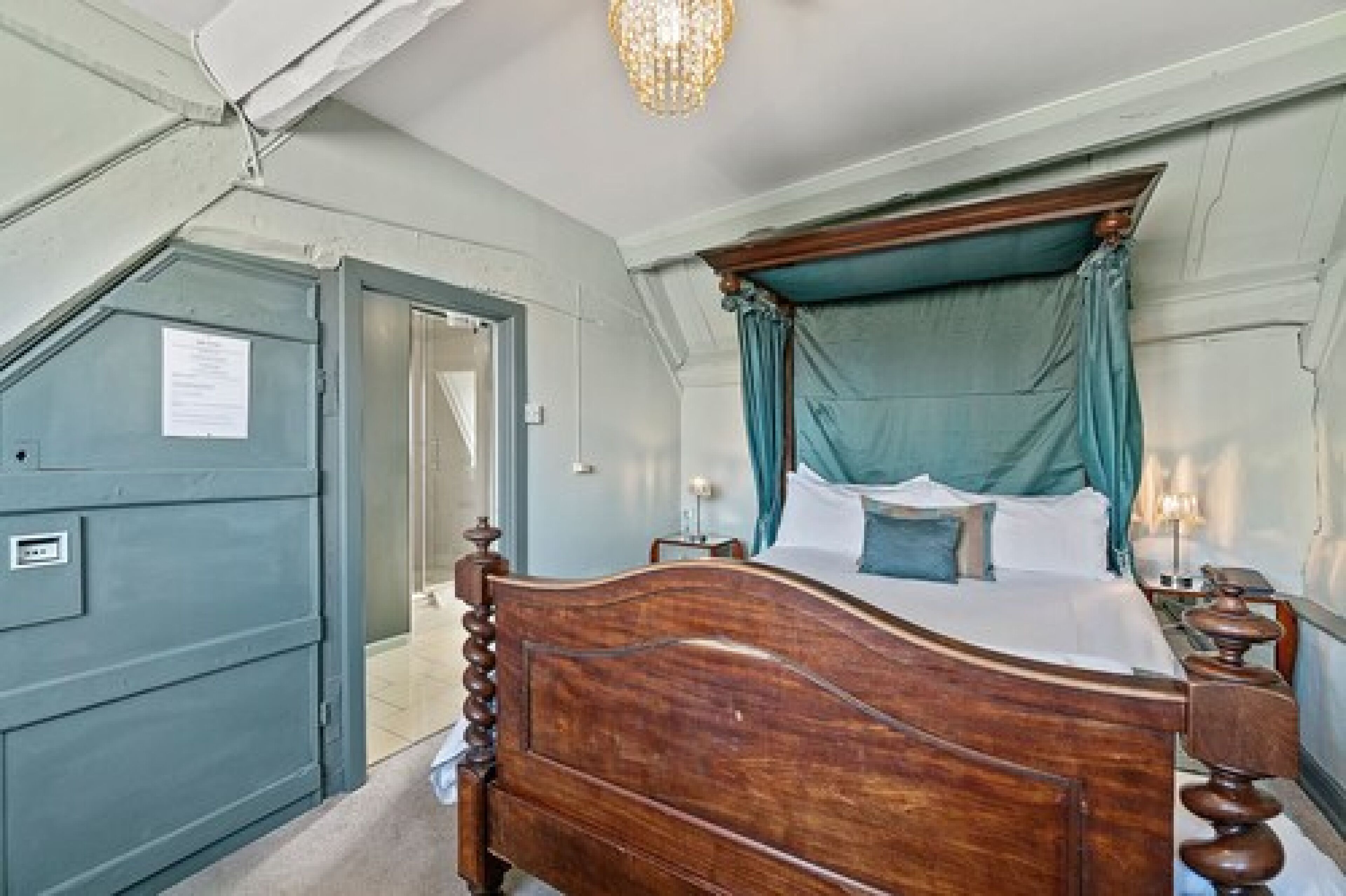 Un dormitorio con cama de madera, dosel verde azulado y candelabro.