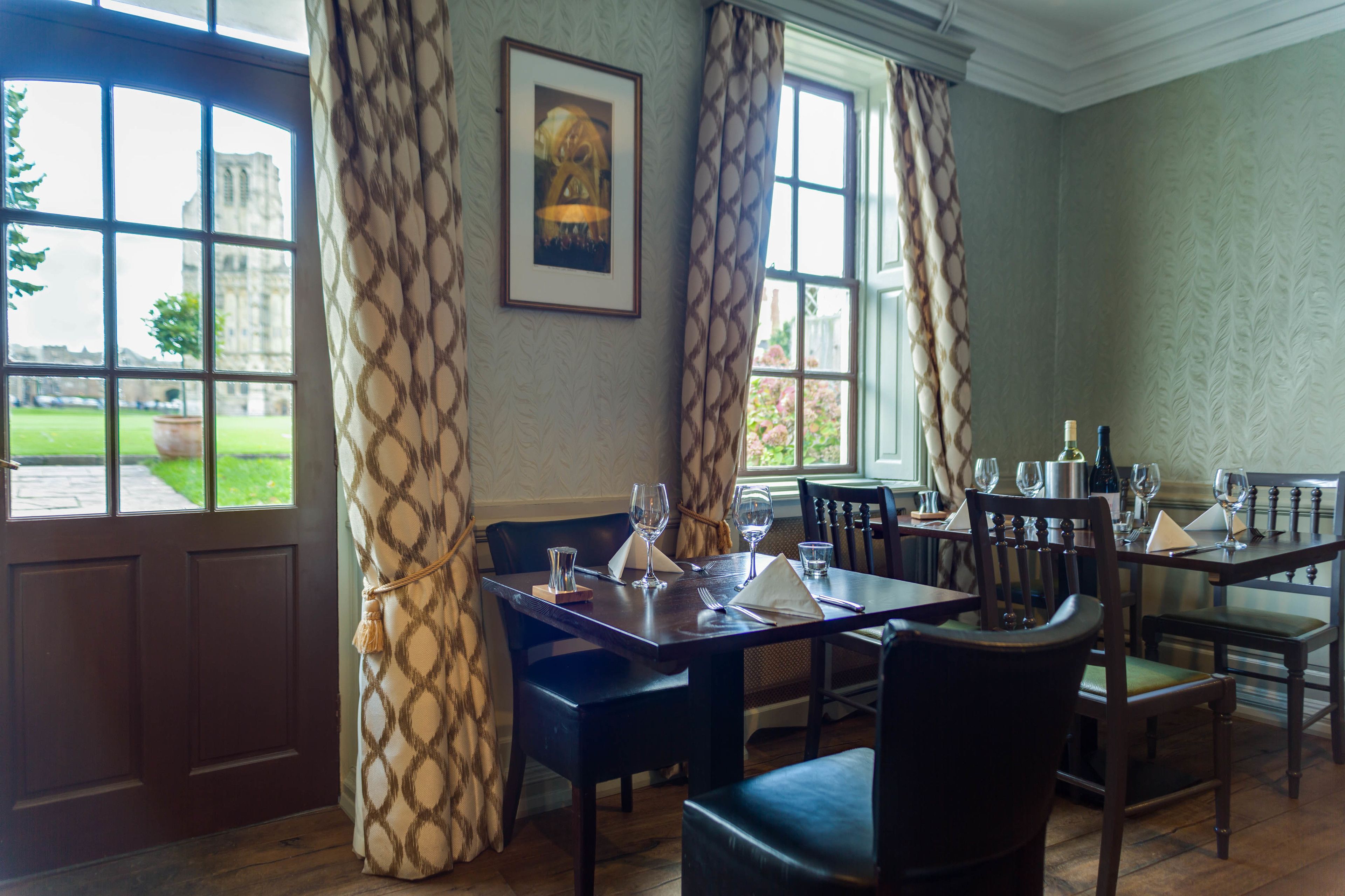 A dining area with a table set for four, a framed picture on the wall, and large windows with curtains.