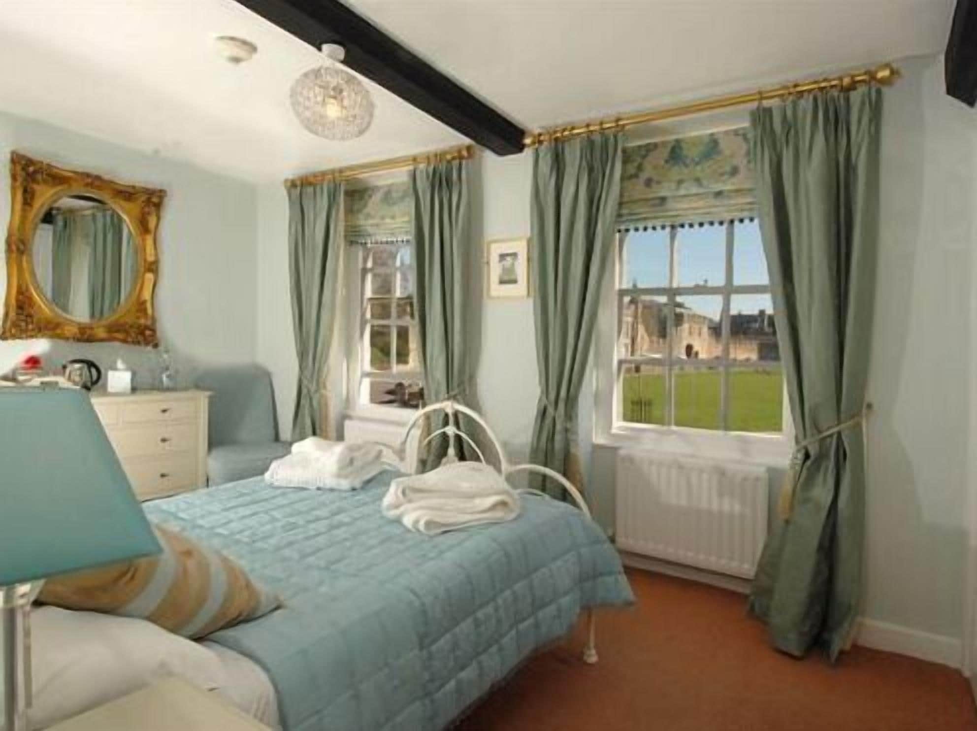 A bedroom with a bed, a dresser, a mirror, and a window with curtains.