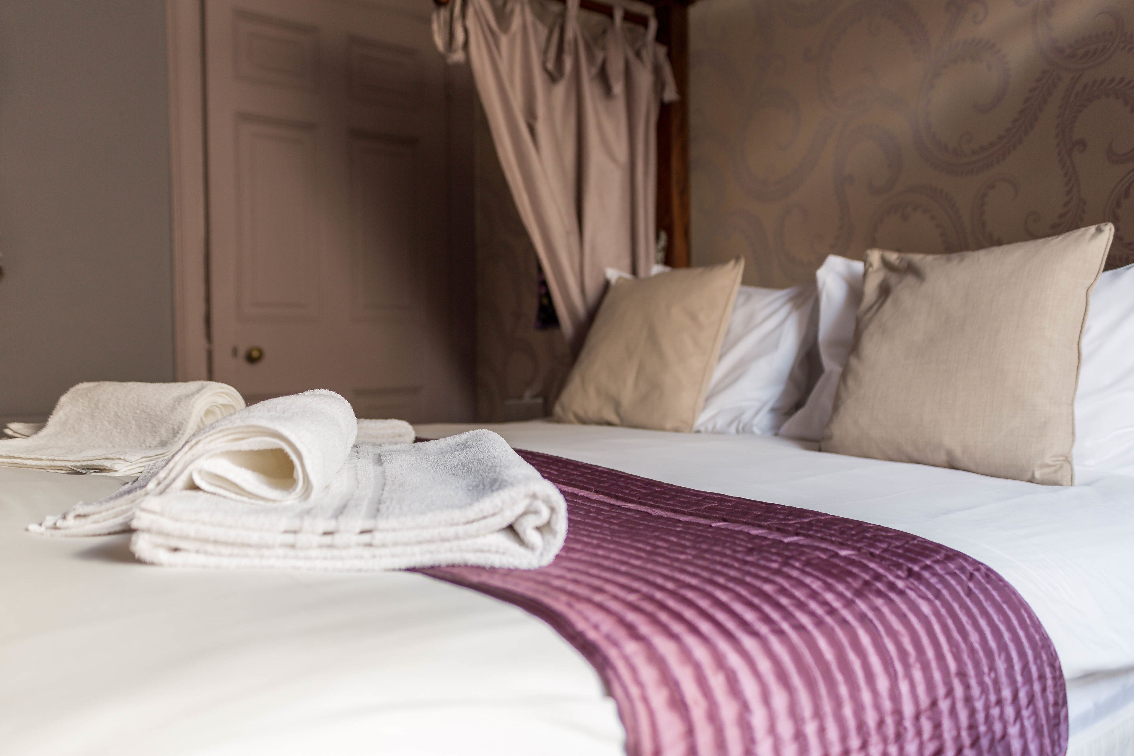 A neatly made bed with a striped blanket, a set of folded towels, and a canopy over the bed.