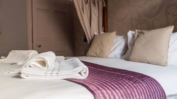 A neatly made bed with a striped blanket, a set of folded towels, and a canopy over the bed.