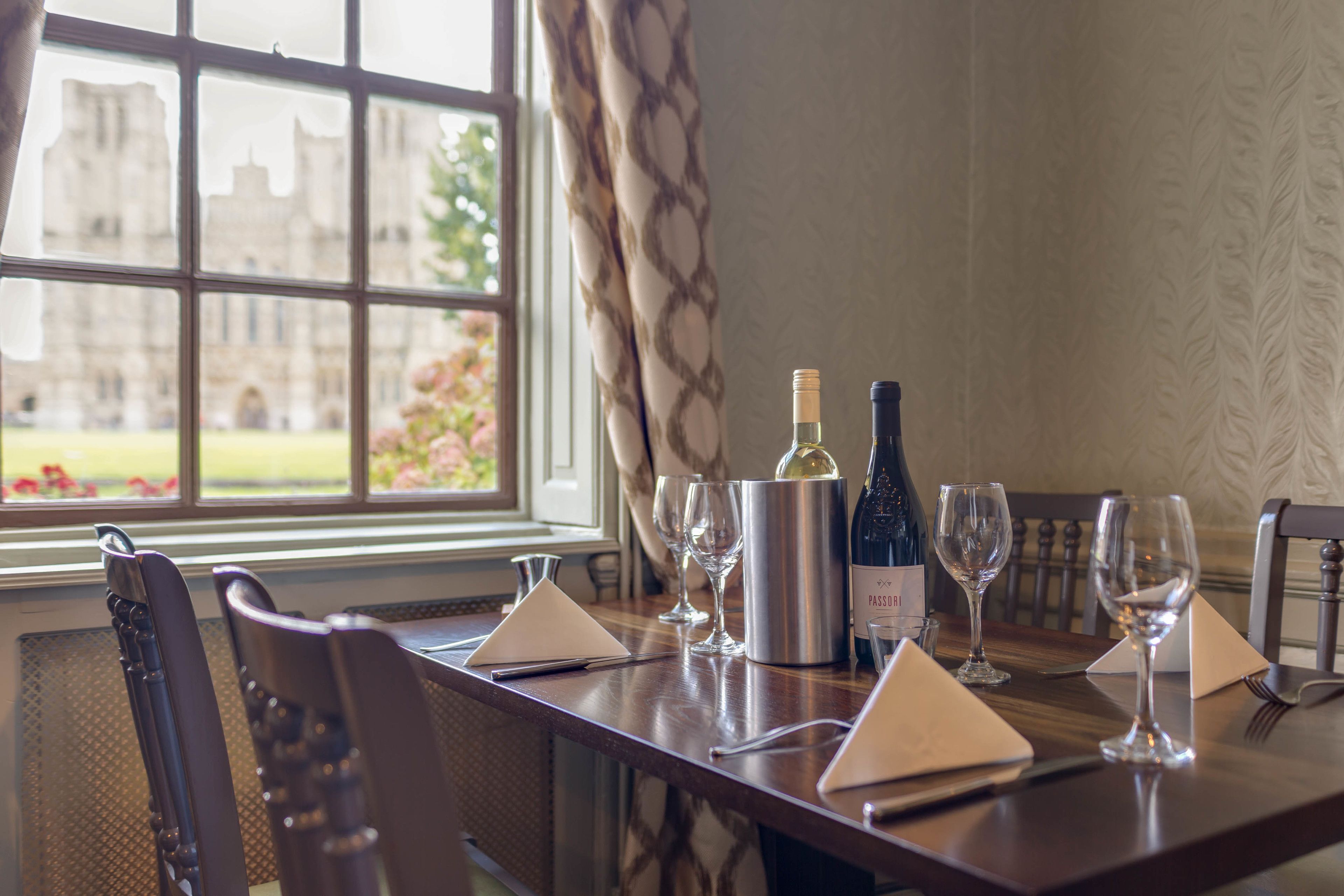 A dining table set with wine glasses, a bottle of wine, and a silver wine cooler.