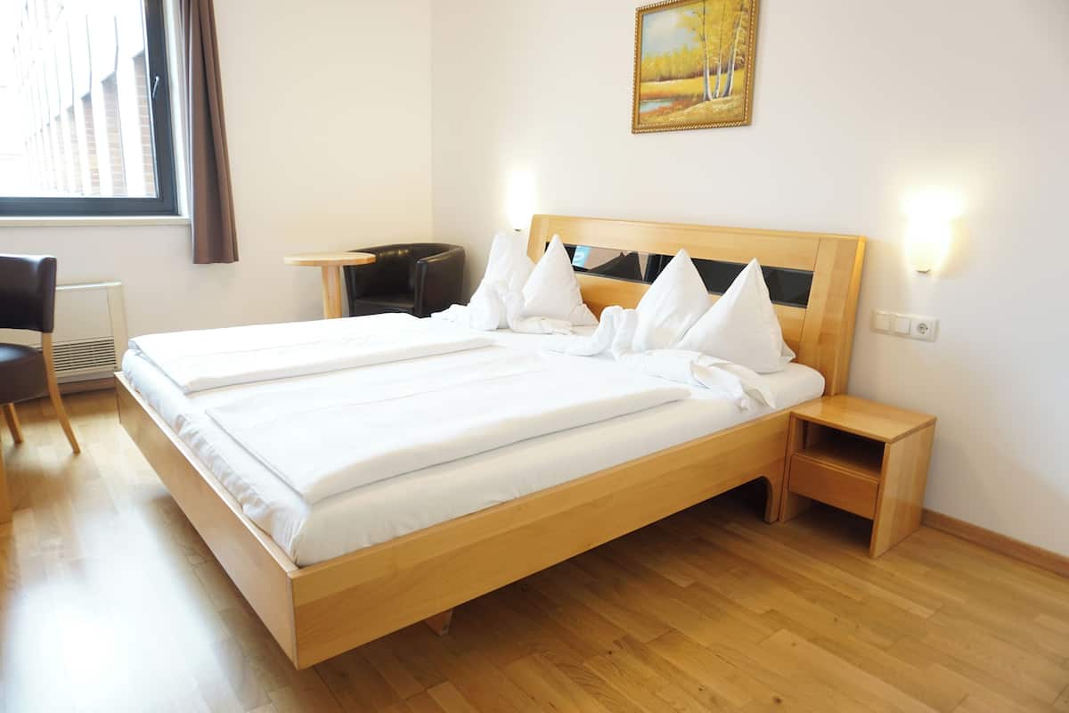 A hotel room with a wooden bed, a desk, a chair, and a painting on the wall.