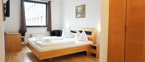 Habitación de hotel con cama de madera, escritorio, silla, televisor, ventana con cortinas y armario.