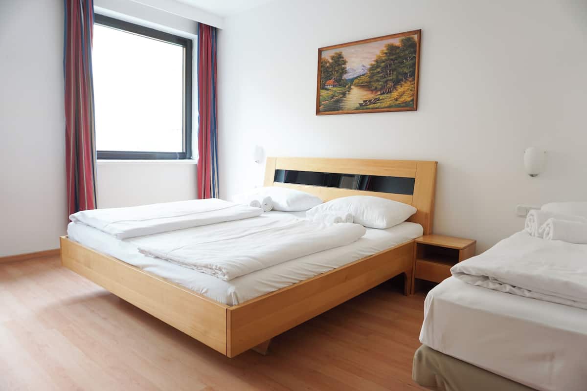 A room with a wooden bed, a nightstand, a painting on the wall, and a window with curtains.