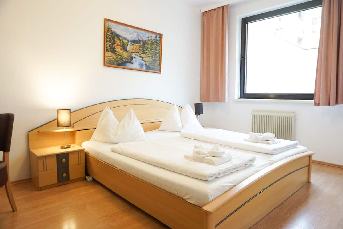 A hotel room with a bed, a nightstand, a lamp, a painting on the wall, and a window with curtains.