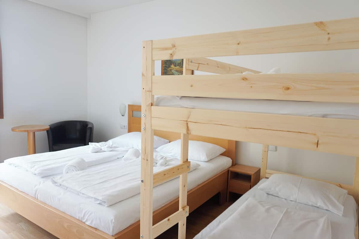 A bunk bed with white bedding, a small bedside table, a chair, and a round table.