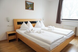 A double bed with white linens and pillows, a nightstand, a wall-mounted light, a painting, and a window with curtains. - Hotel Kaffeemühle (Vienna)