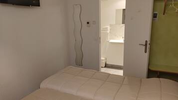 Un dormitorio con una cama, una puerta que da a un baño y un televisor montado en la pared.