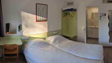 Habitación de hotel pequeña con cama, escritorio, silla y baño visible a través de una puerta abierta.