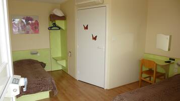 Ein Zimmer mit zwei Betten, einem Schreibtisch, einem Stuhl, einem Kleiderschrank und einer Schmetterlingsdekoration an der Tür.