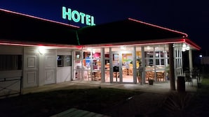Ein Hotel mit leuchtendem Neonzeichen, Glastüren und einer Terrasse mit Tischen und Stühlen.