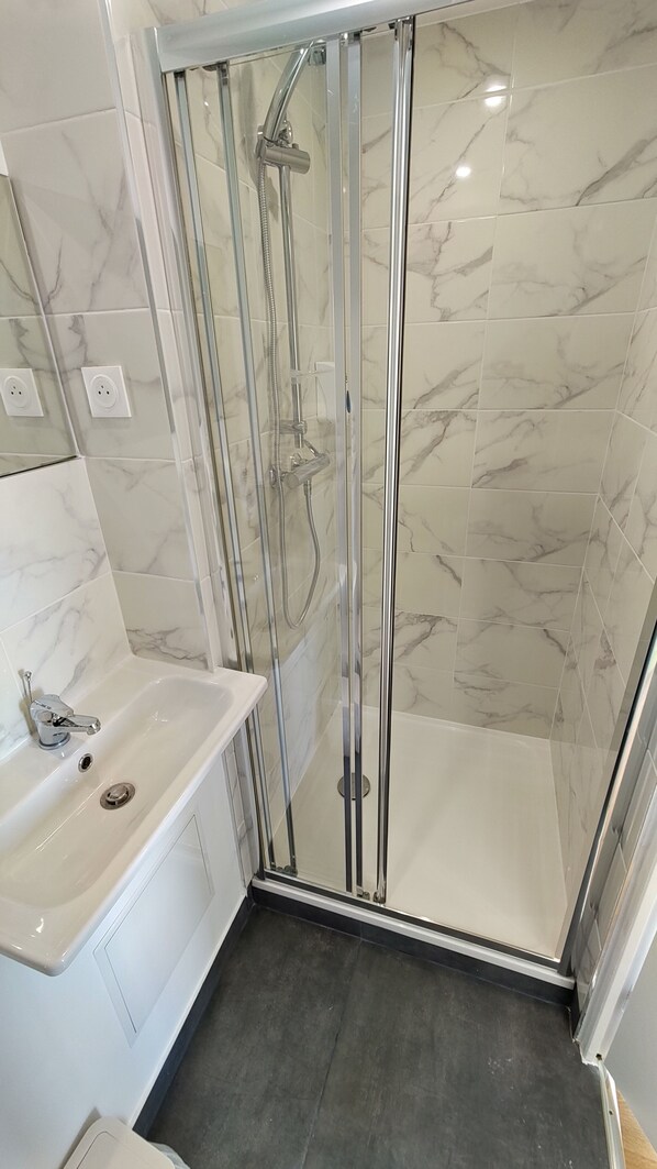 Un baño moderno con ducha de vidrio, lavamanos blanco y paredes con azulejos de mármol.