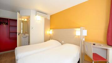 Een hotelkamer met twee bedden, een bureau, een stoel, een spiegel en een rode garderobe.