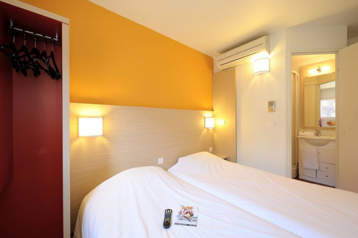 Hotellihuone, jossa on sänky, seinään asennettu ilmastointilaite, peili ja ovi, joka johtaa kylpyhuoneeseen.