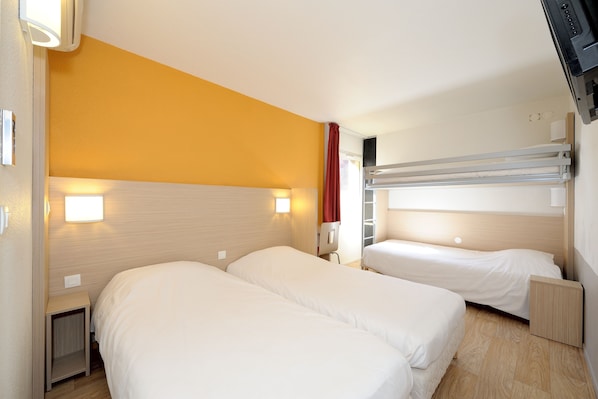 A hotel room with two single beds, a bunk bed, a small desk, and a wall-mounted TV.