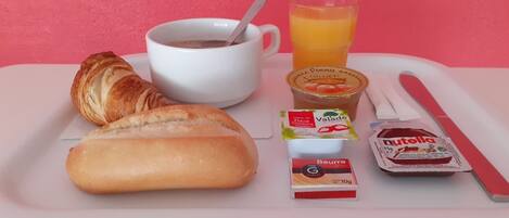 Bandeja de desayuno con cruasanes, una taza de café, un vaso de zumo de naranja, un paquete de Nutella y crema de queso Beurre.