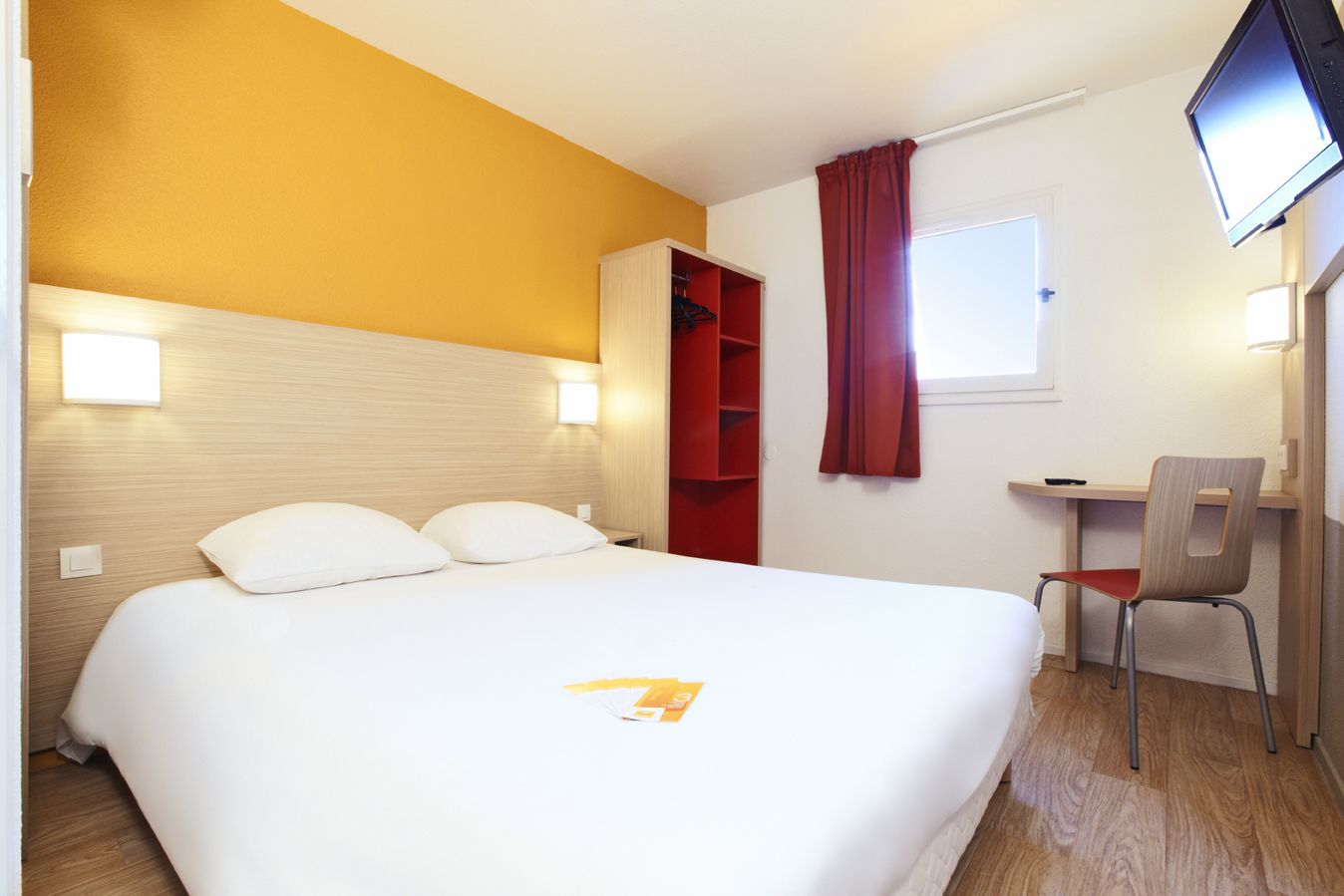 A hotel room with a bed, a desk, a chair, and a TV.
