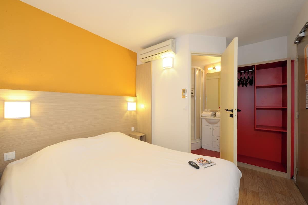 A hotel room with a large bed, bedside lamps, a red wardrobe, and an open door leading to a bathroom.