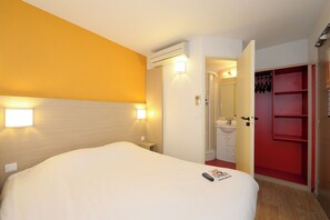 A hotel room with a large bed, bedside lamps, a red wardrobe, and an open door leading to a bathroom.