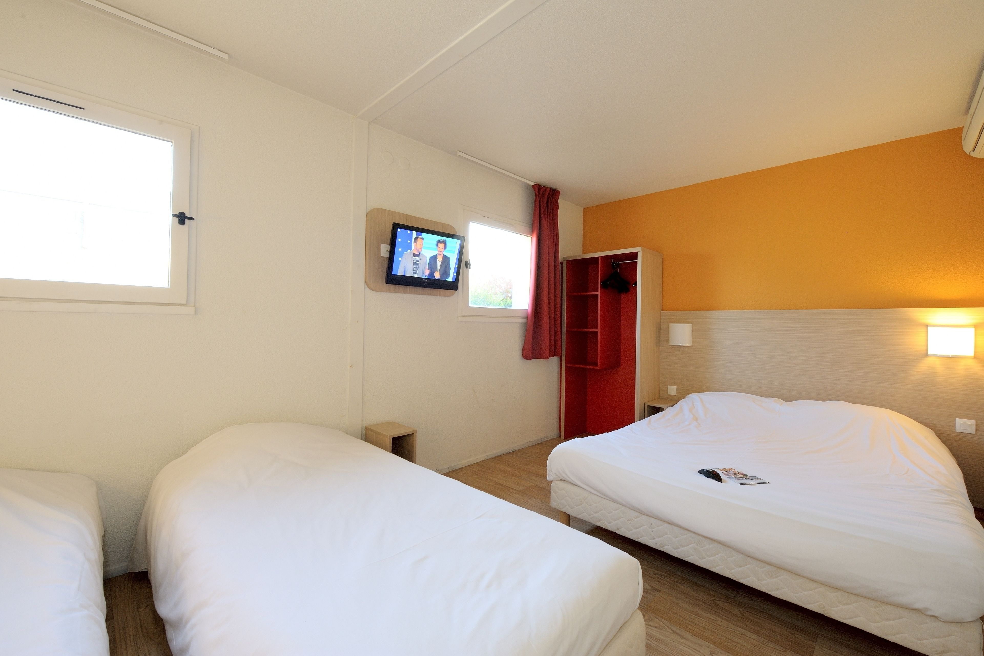 Een hotelkamer met twee bedden, een televisie aan de muur en een rode garderobe.