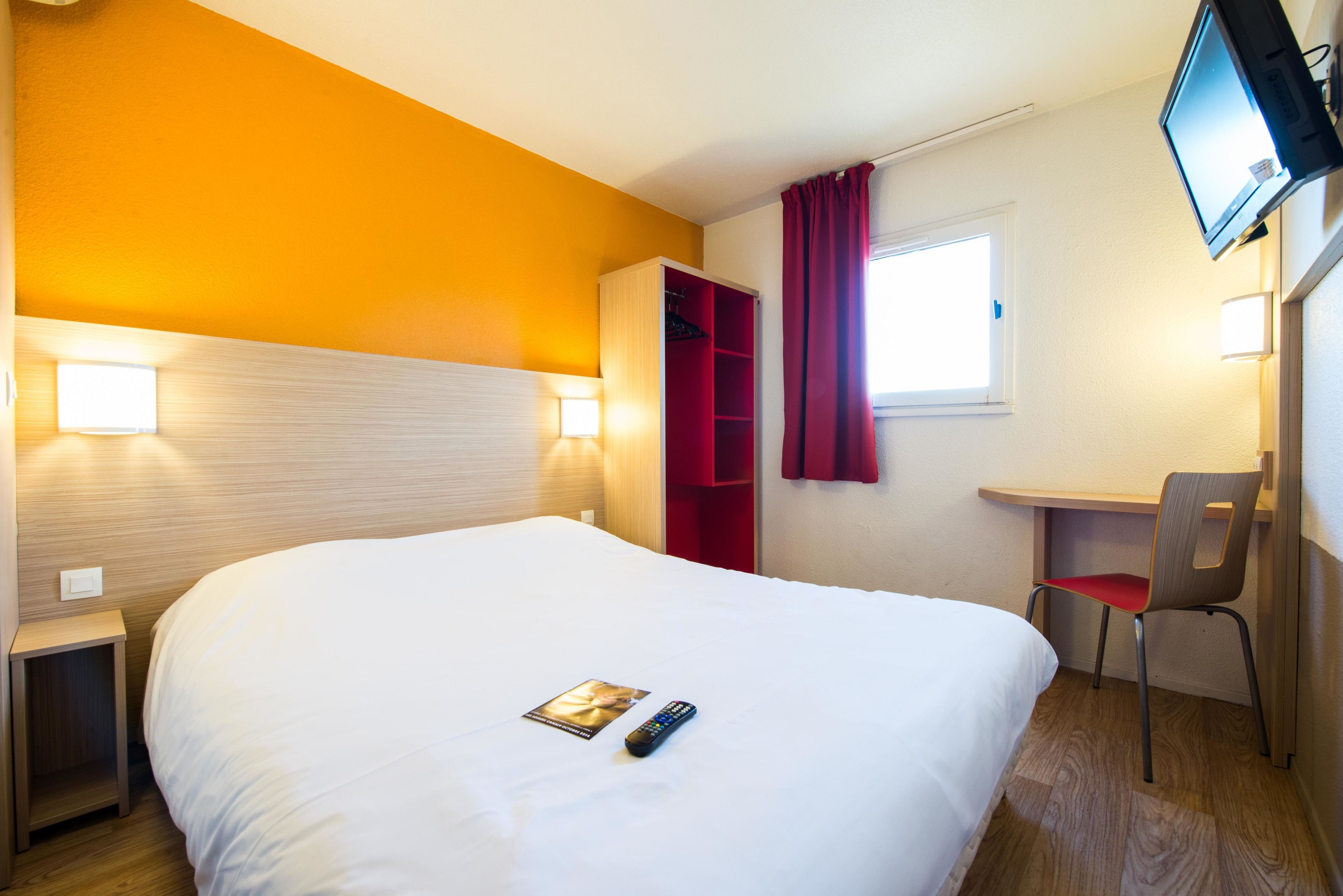 Habitación de hotel con una cama grande, un escritorio con silla, un televisor montado en la pared y una ventana con cortinas.