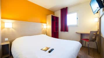 Ein Hotelzimmer mit einem großen Bett, einem Schreibtisch mit Stuhl, einem an der Wand befestigten Fernseher und einem Fenster mit Vorhängen.