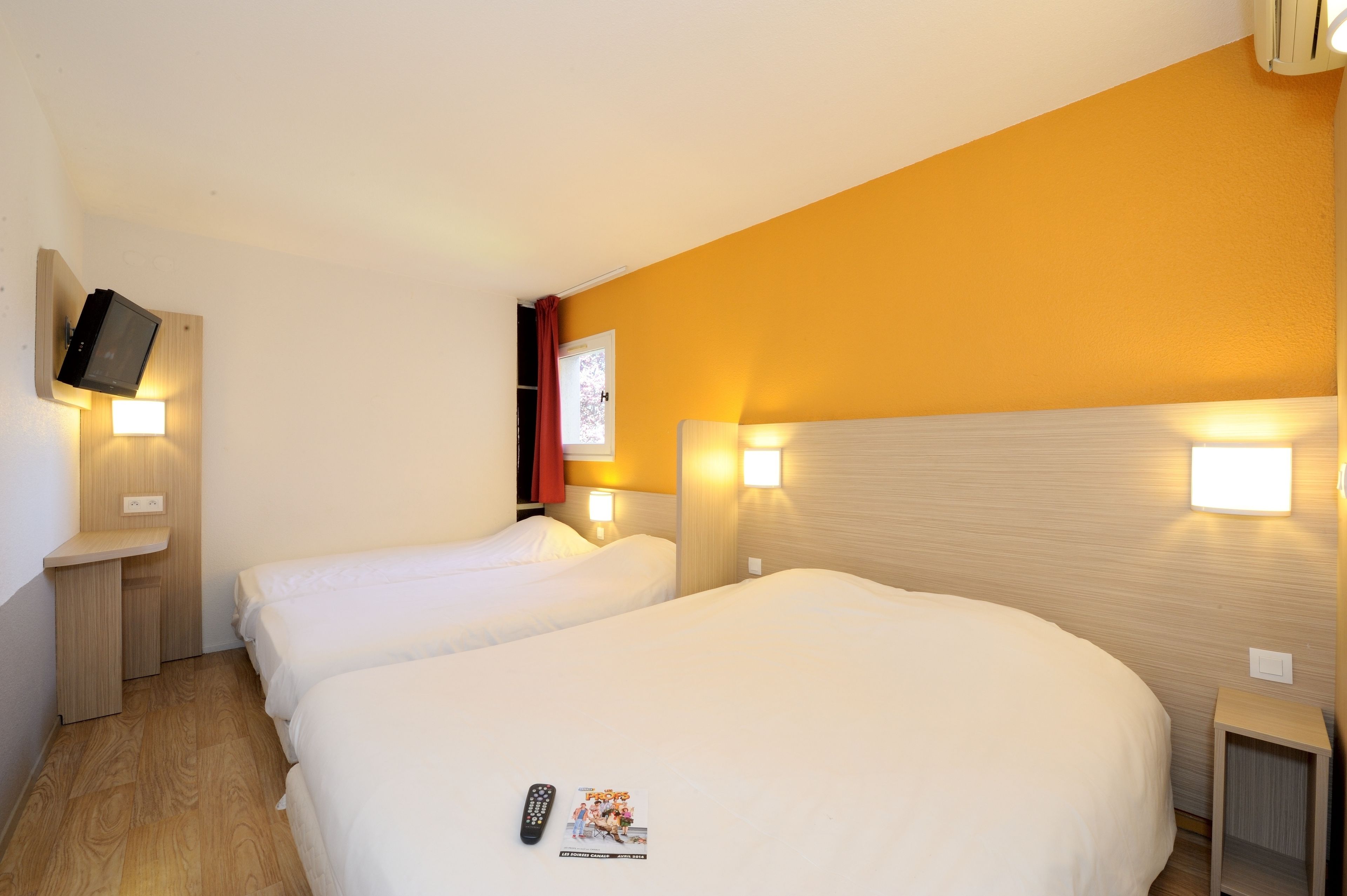 A hotel room with two beds, a TV mounted on the wall, and bedside lamps.