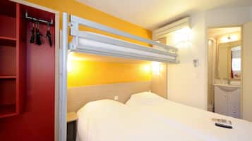 Quarto de hotel com beliche, um guarda-roupa vermelho, mesa de cabeceira e banheiro visível por uma porta aberta.